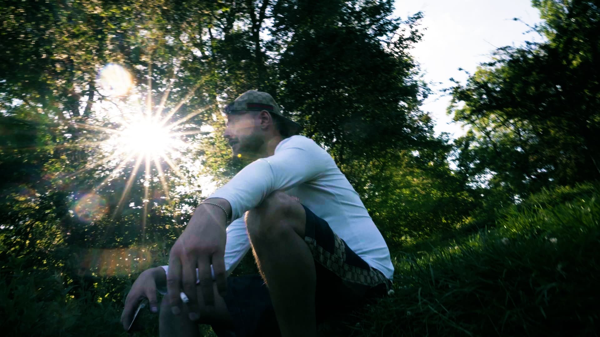 Rapper sitting in the grass with the sun flaring through the trees during a backlit music video shoot