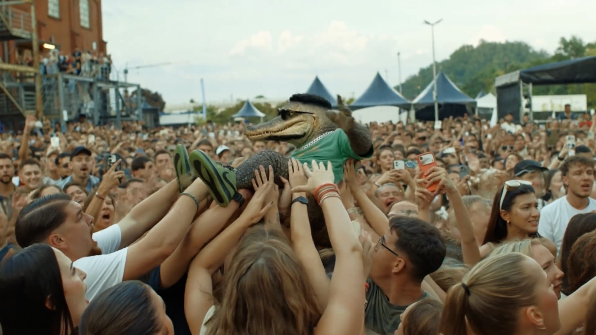 Person in a crocodile costume crowd surfing at a festival during the Killy Manjaro Euromix video shoot