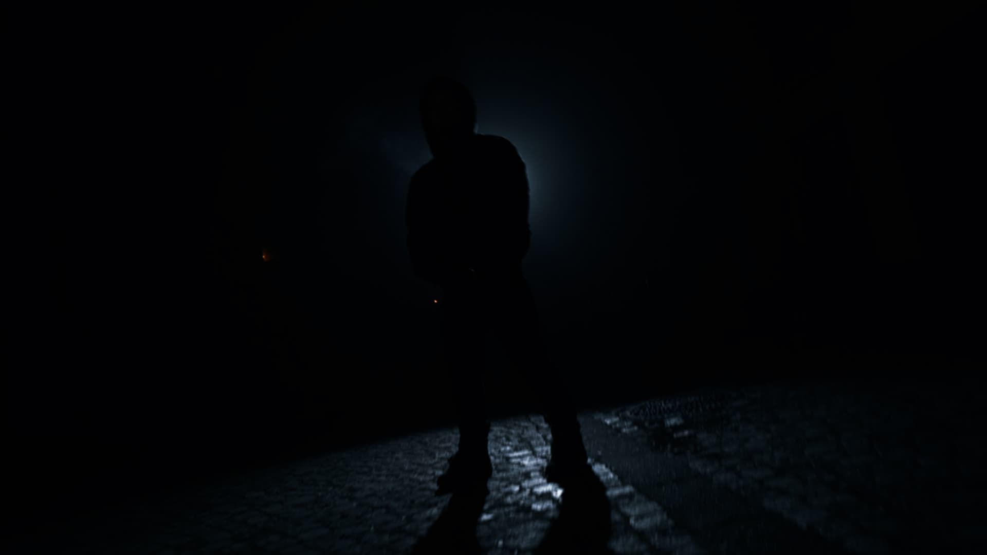 Silhouette of a person backlit on wet cobblestones during a night music video shoot