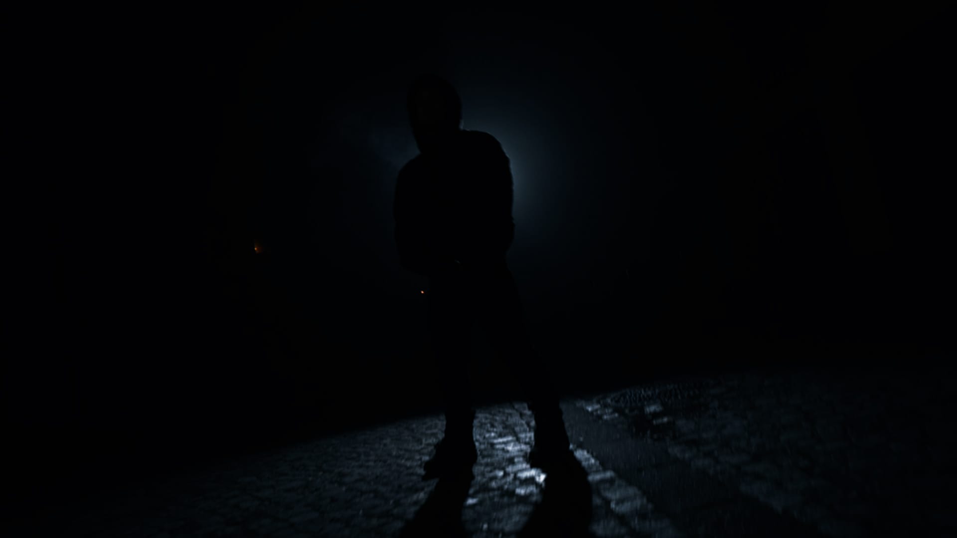 Silhouette of a person backlit on wet cobblestones during a night music video shoot
