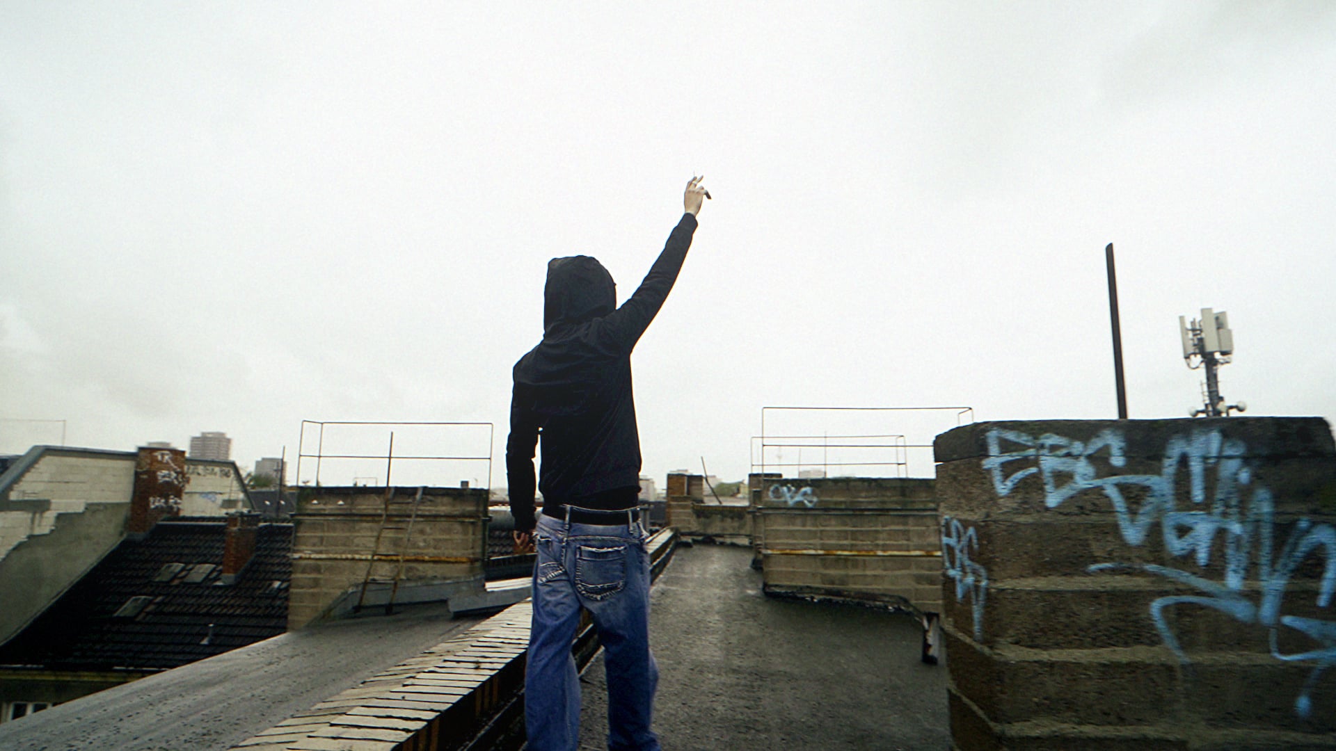 Silhouette with a raised arm on a rooftop above the city, a scene from a Lossvisuals rap music video shoot